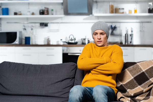 Person sitting on couch with hat, freezing.