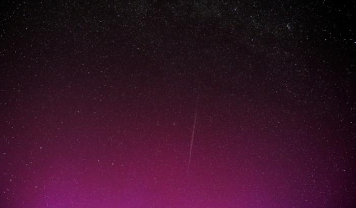Une photo en pose longue montre une traînée laissée par un groupe de satellites Starlink de SpaceX, dans un ciel illuminé par des aurores boréales pendant la pluie annuelle d'étoiles filantes des Perséides, le 12 août 2024 à Wigry, en Pologne