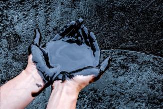 Zwei Hände in Erdöl eingetaucht.