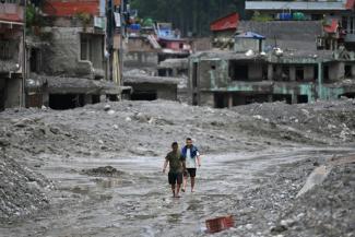 Des habitants traversent, le 30 août 2026, une rue ensevelie sous des tonnes de boue du centre de Trishuli, au Népal, victime d'une crue dévastatrice